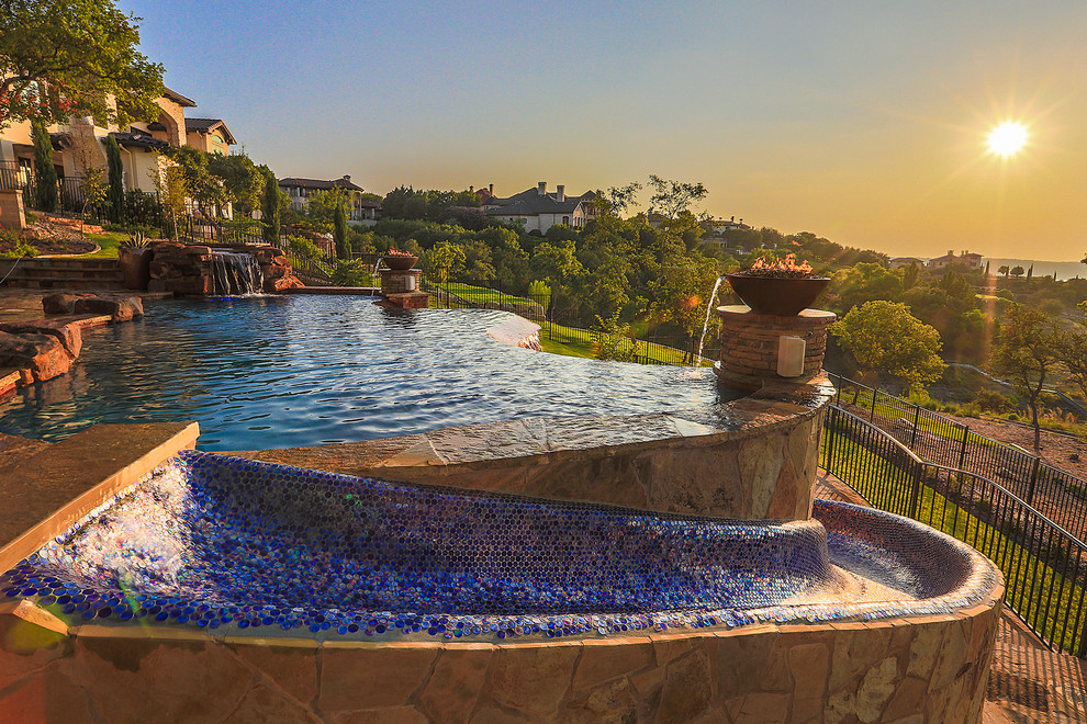 Diseño de piscina con tobogán infinita mediterránea grande a medida en patio trasero con adoquines de piedra natural