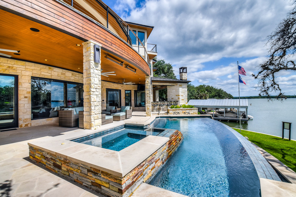 Immagine di una grande piscina a sfioro infinito minimal personalizzata dietro casa con una vasca idromassaggio e pavimentazioni in pietra naturale