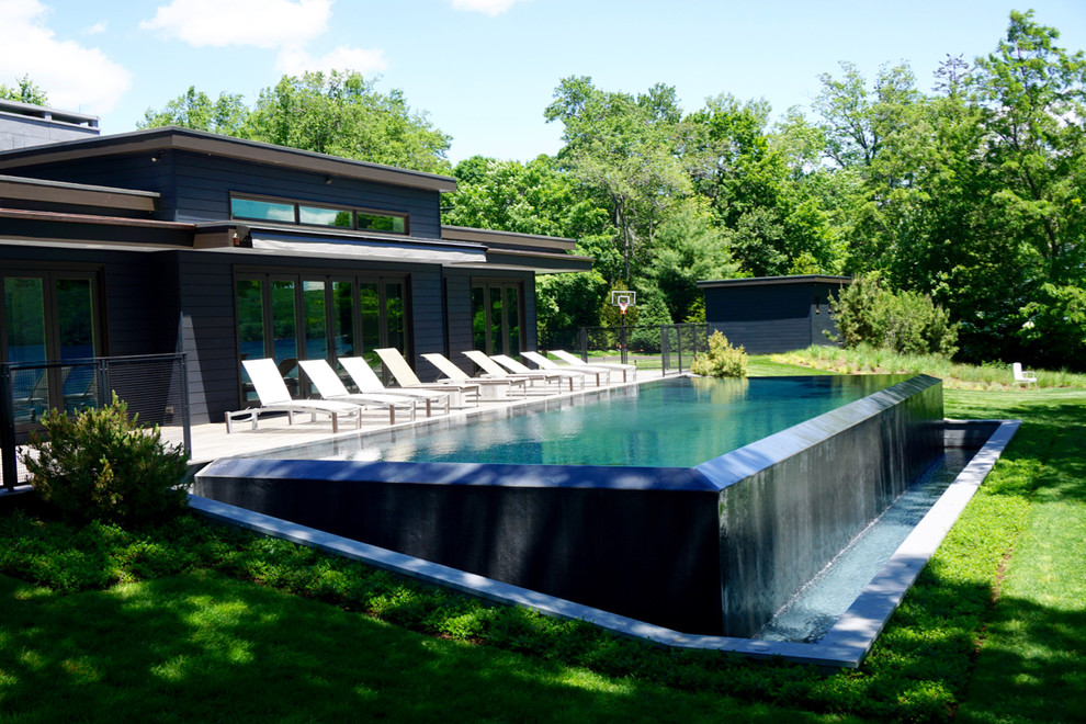 Aménagement d'une grande piscine à débordement et latérale moderne rectangle avec une terrasse en bois.