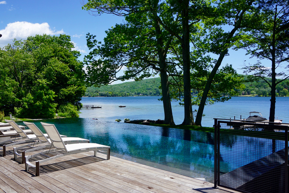 Inspiration pour une grande piscine à débordement et latérale minimaliste rectangle avec une terrasse en bois.