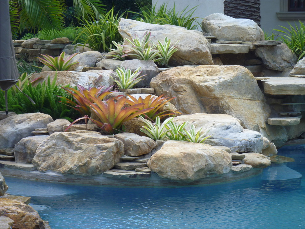 Diseño de piscina con fuente alargada tradicional de tamaño medio a medida en patio trasero con adoquines de piedra natural