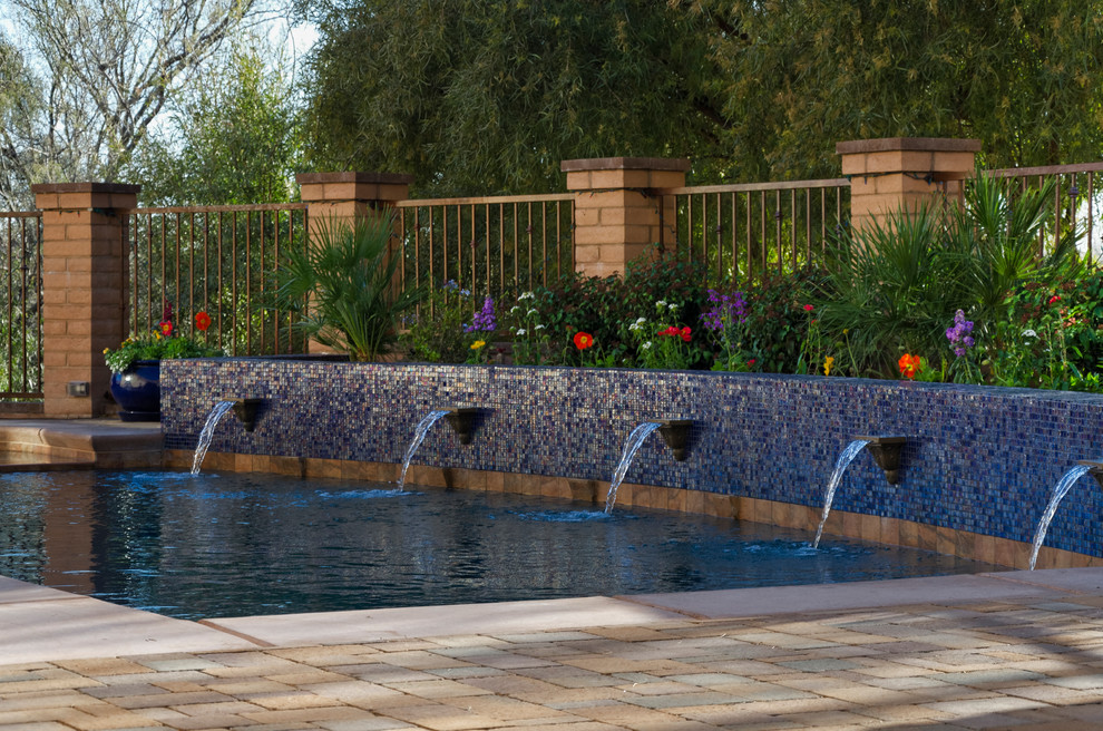 На фото: большой прямоугольный бассейн на заднем дворе в стиле фьюжн с фонтаном и мощением тротуарной плиткой с