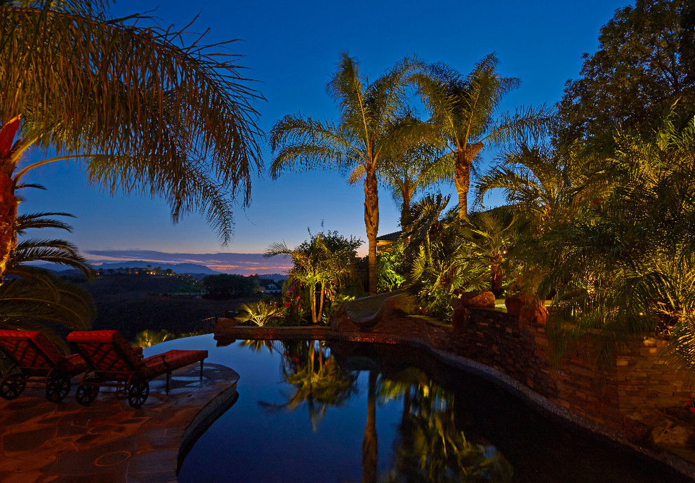 Ejemplo de piscina con tobogán tropical grande tipo riñón en patio trasero con adoquines de piedra natural