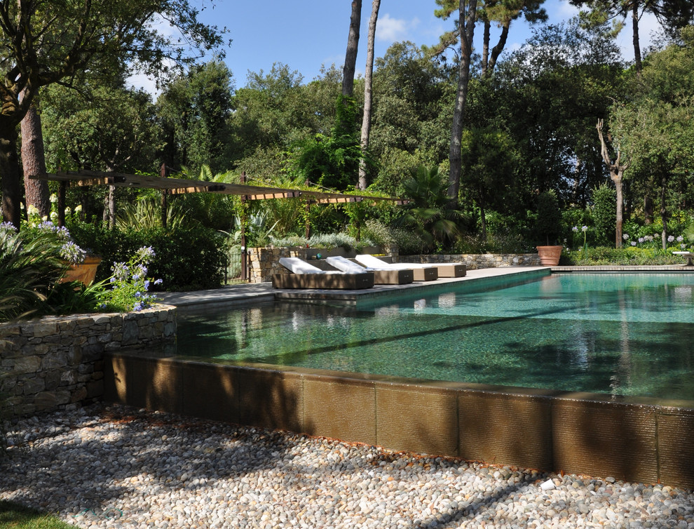 Immagine di un'ampia piscina a sfioro infinito minimal rettangolare con una dépendance a bordo piscina e pavimentazioni in pietra naturale