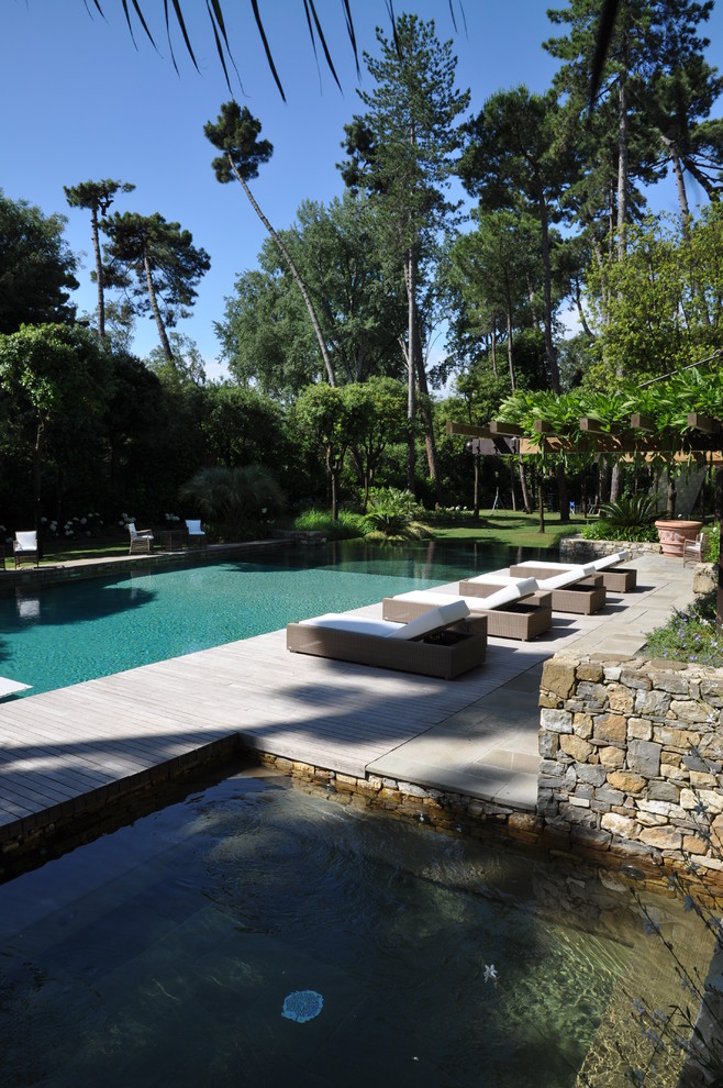 Ispirazione per un'ampia piscina a sfioro infinito minimal rettangolare con una dépendance a bordo piscina e pavimentazioni in pietra naturale
