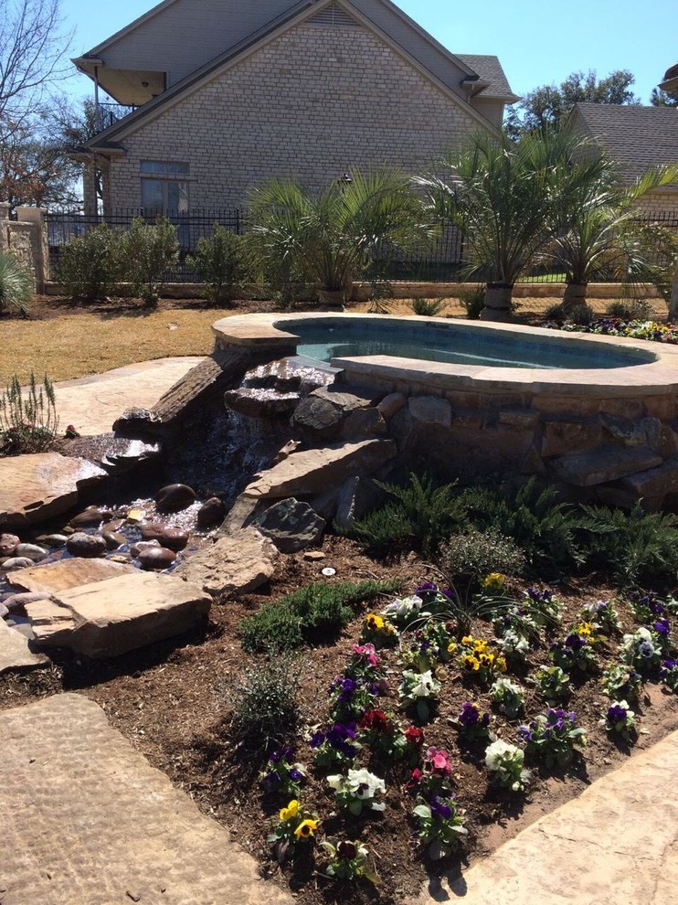 Immagine di una grande piscina stile americano personalizzata dietro casa con una vasca idromassaggio e pavimentazioni in pietra naturale