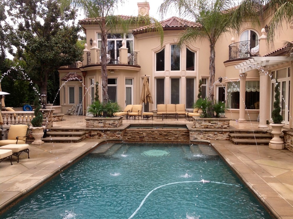 Diseño de piscina con fuente alargada mediterránea rectangular en patio trasero con adoquines de piedra natural