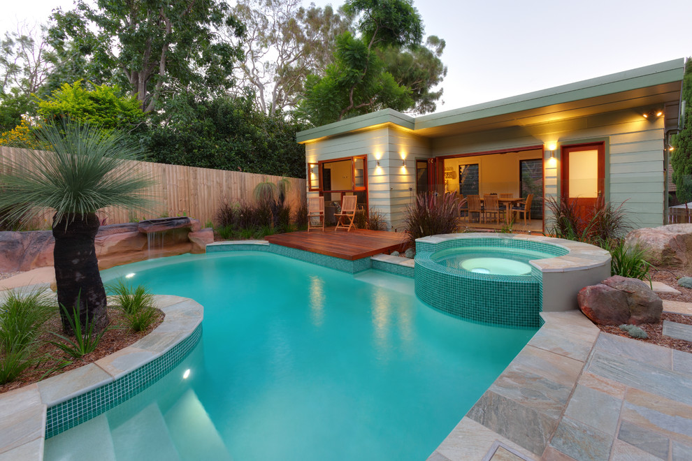 Идея дизайна: бассейн произвольной формы на заднем дворе в современном стиле с покрытием из каменной брусчатки и забором