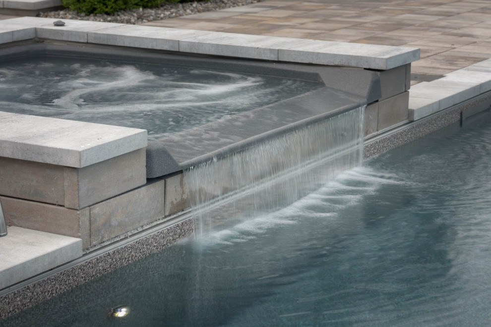 Expansive modern back rectangular lengths swimming pool in Toronto with a water feature and natural stone paving.