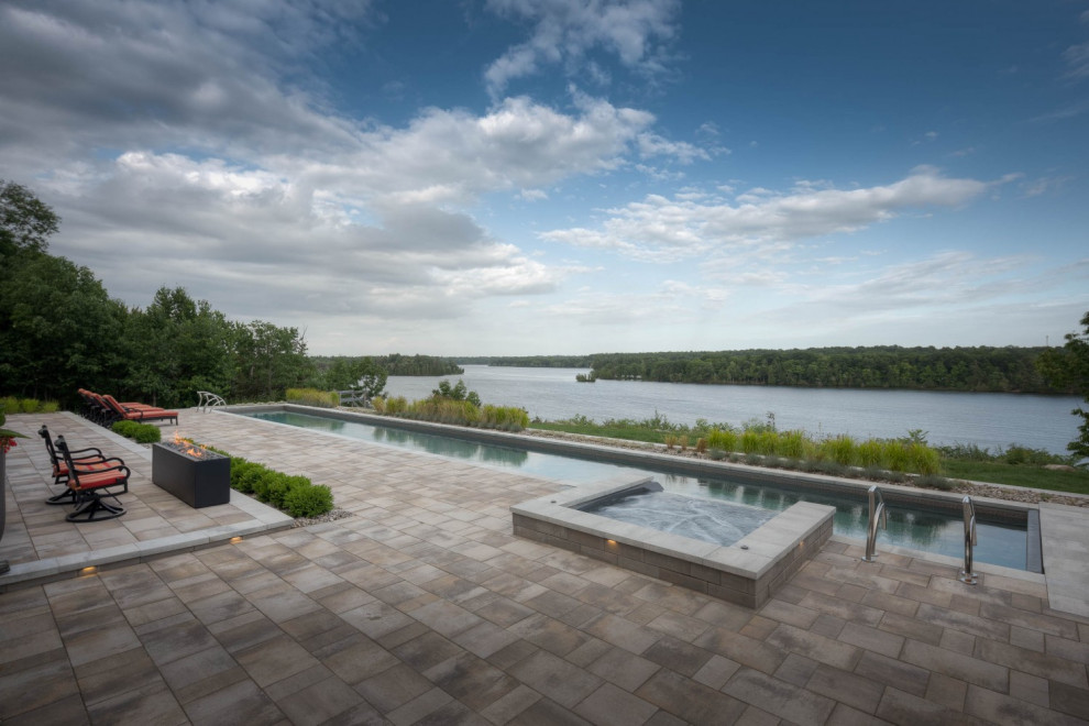 Foto di un'ampia piscina monocorsia minimalista rettangolare dietro casa con una vasca idromassaggio e pavimentazioni in pietra naturale