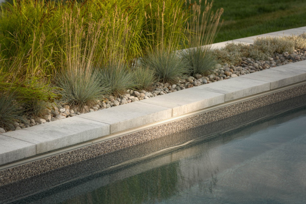 Modelo de piscina alargada moderna extra grande rectangular en patio trasero con adoquines de piedra natural