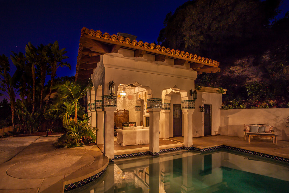 На фото: большой бассейн произвольной формы на заднем дворе в средиземноморском стиле с покрытием из бетонных плит и домиком у бассейна
