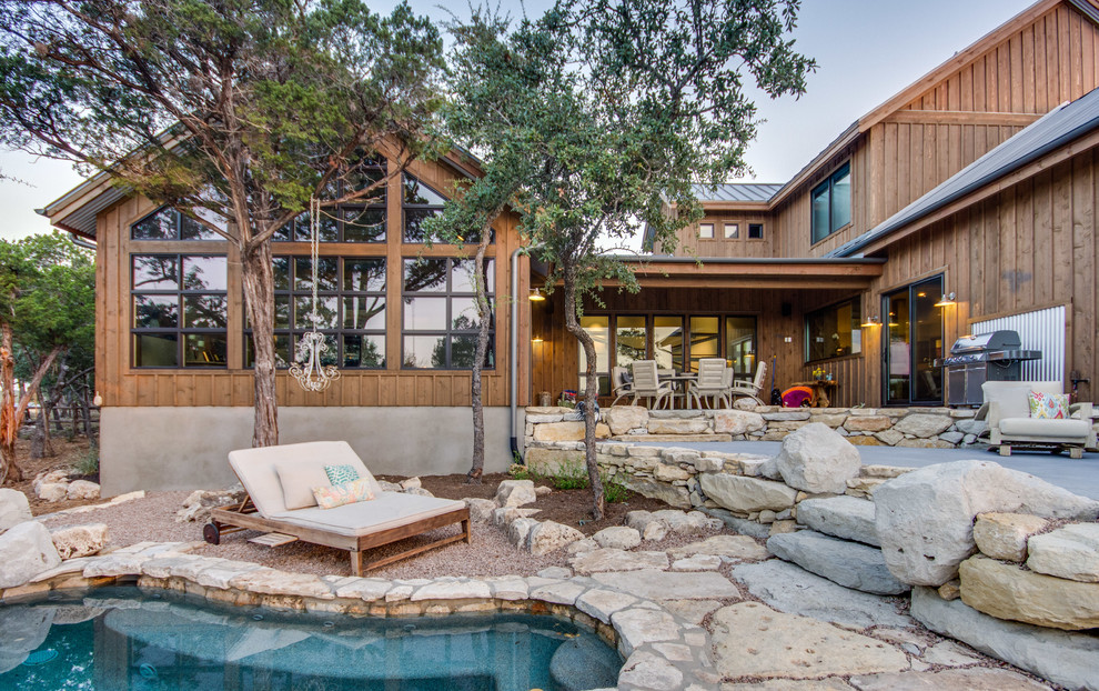 This is an example of a large eclectic back custom shaped natural swimming pool in Austin with a pool house and natural stone paving.