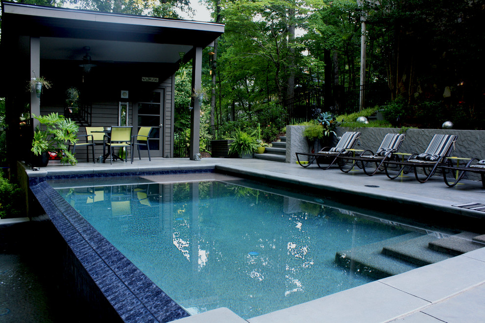 Modelo de casa de la piscina y piscina infinita contemporánea de tamaño medio rectangular en patio trasero con adoquines de hormigón