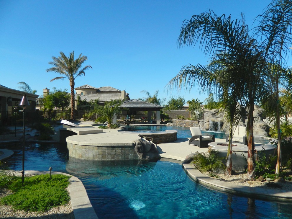 Ejemplo de piscina natural mediterránea grande a medida en patio trasero con adoquines de piedra natural