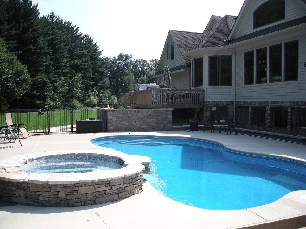 Expansive modern back custom shaped swimming pool in Other with concrete slabs.