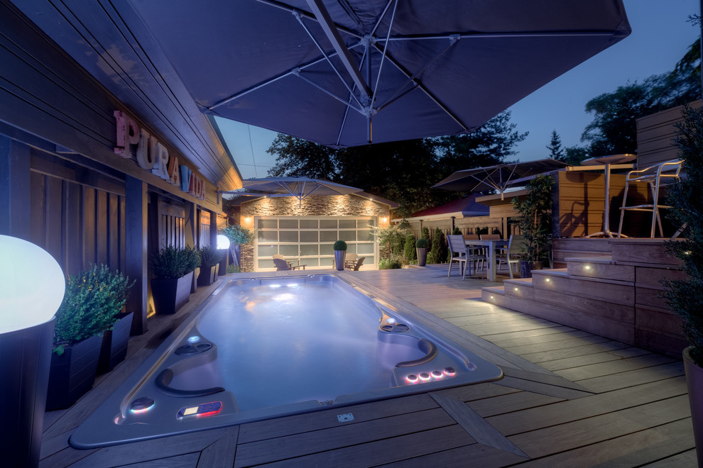 Пример оригинального дизайна: огромный прямоугольный бассейн на заднем дворе в стиле модернизм с джакузи и настилом