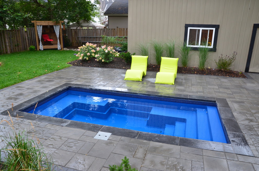 Modelo de piscina contemporánea pequeña rectangular en patio trasero con adoquines de hormigón
