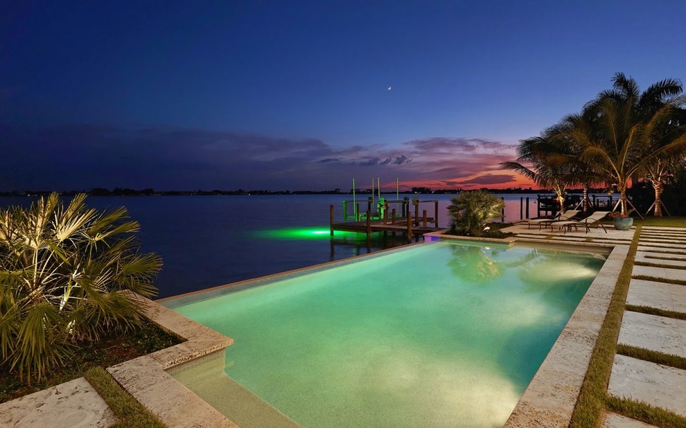 Immagine di una grande piscina a sfioro infinito tropicale rettangolare dietro casa con pavimentazioni in pietra naturale