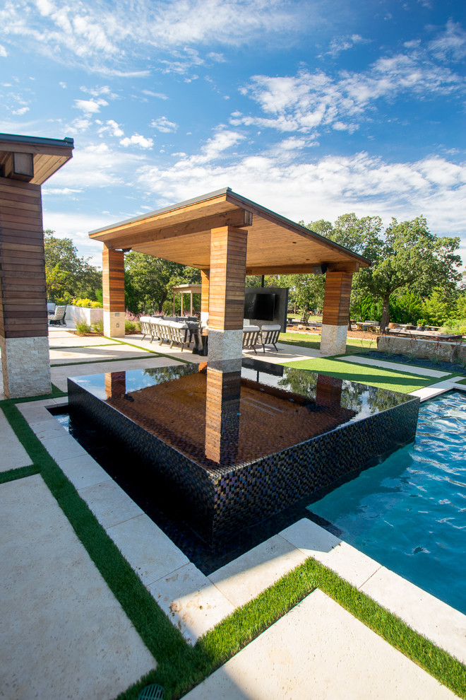 Expansive classic back custom shaped infinity swimming pool in Dallas with a water feature and natural stone paving.