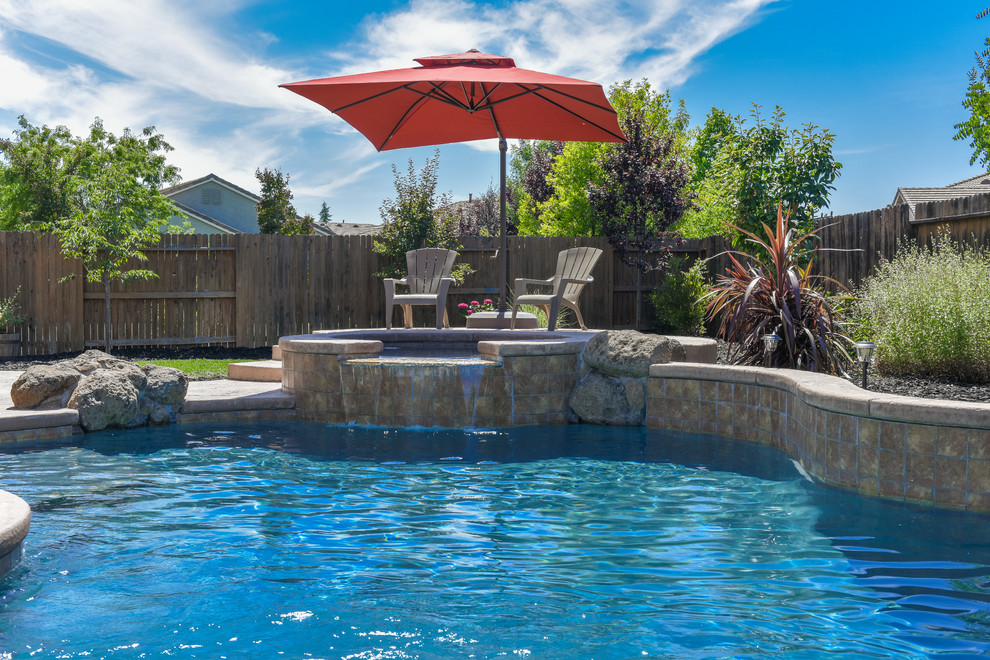 Bild på en stor tropisk njurformad pool på baksidan av huset, med spabad och naturstensplattor