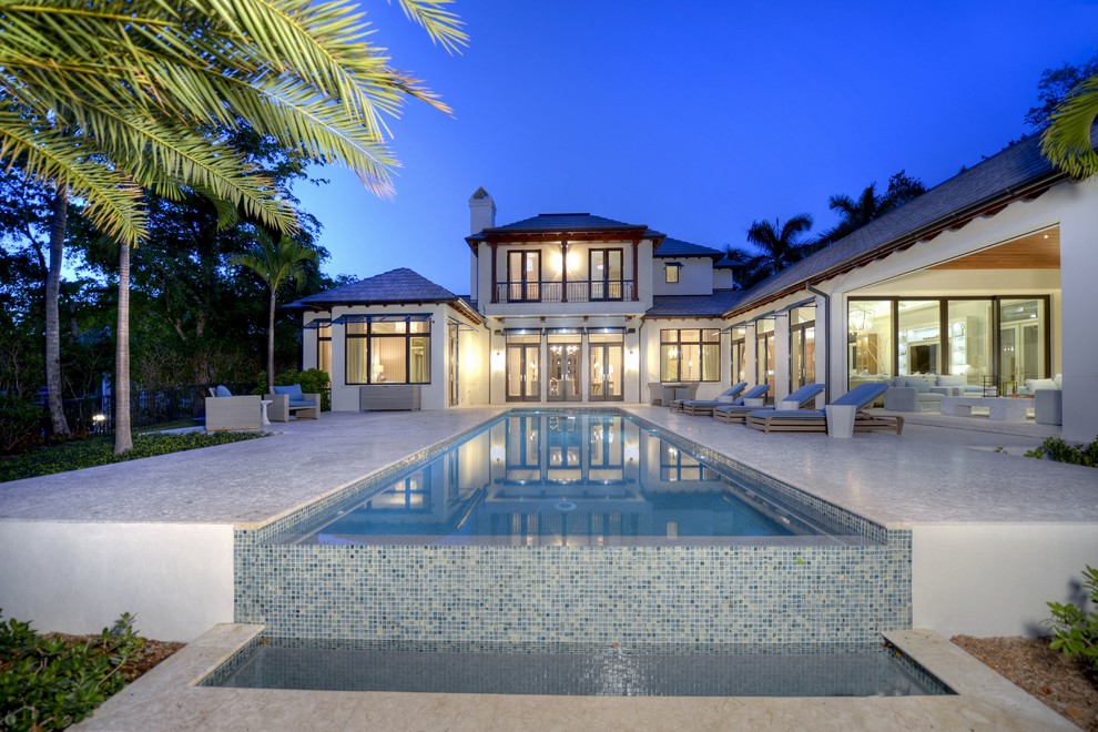 Diseño de piscina infinita exótica extra grande rectangular en patio trasero con suelo de baldosas