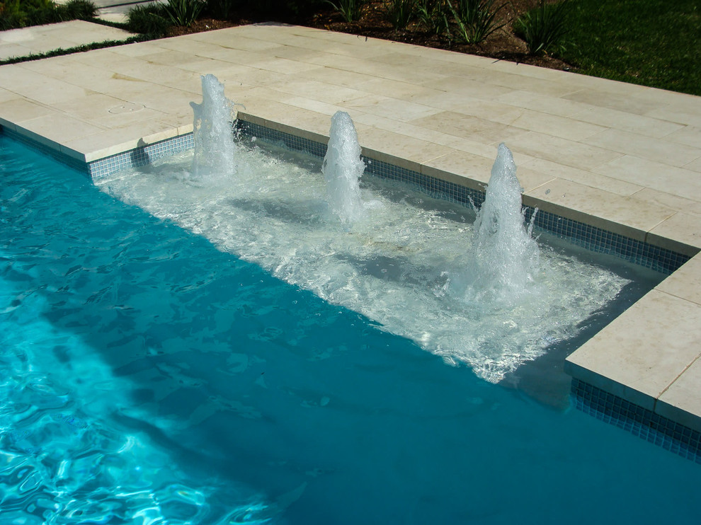 Immagine di una piscina contemporanea rettangolare di medie dimensioni e dietro casa con fontane e pavimentazioni in pietra naturale
