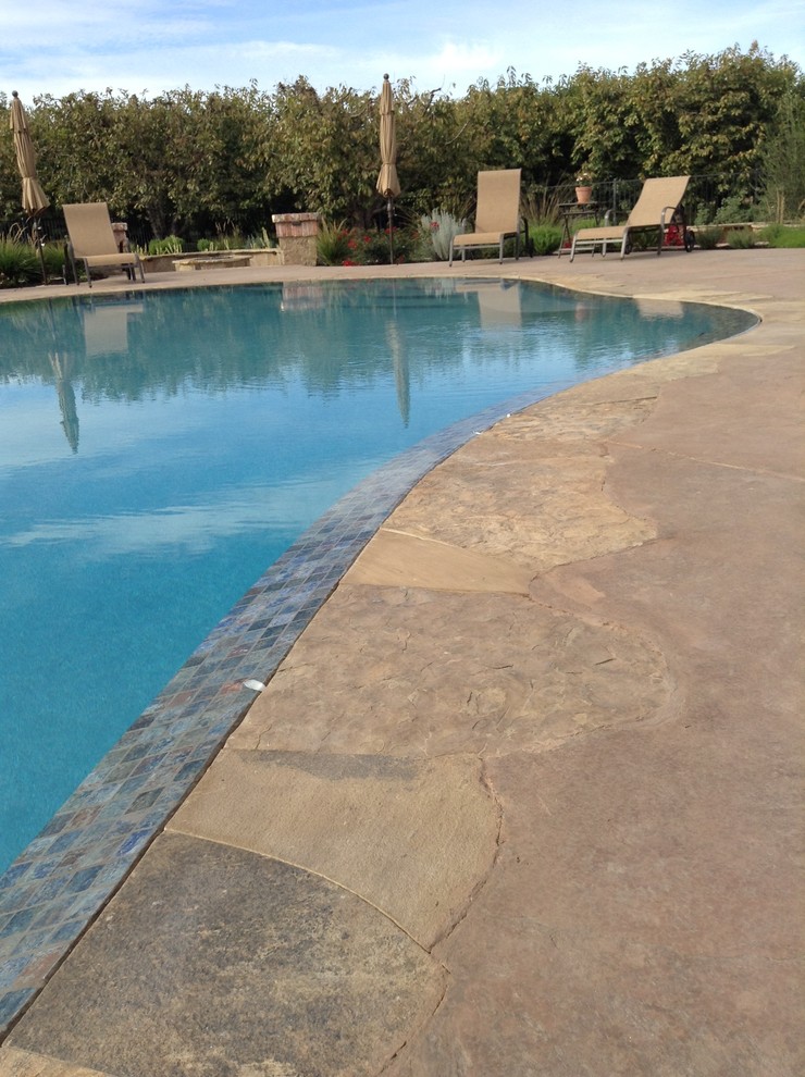 Cette image montre une piscine à débordement et arrière chalet sur mesure avec un point d'eau et du béton estampé.