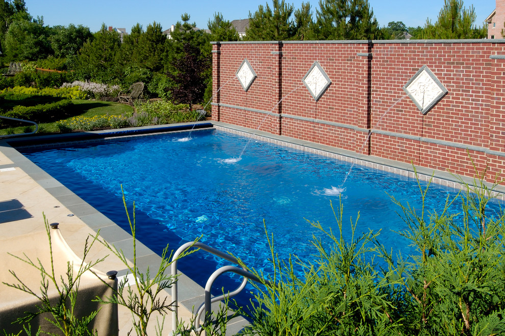 Modelo de piscina alargada mediterránea de tamaño medio rectangular en patio trasero con adoquines de piedra natural