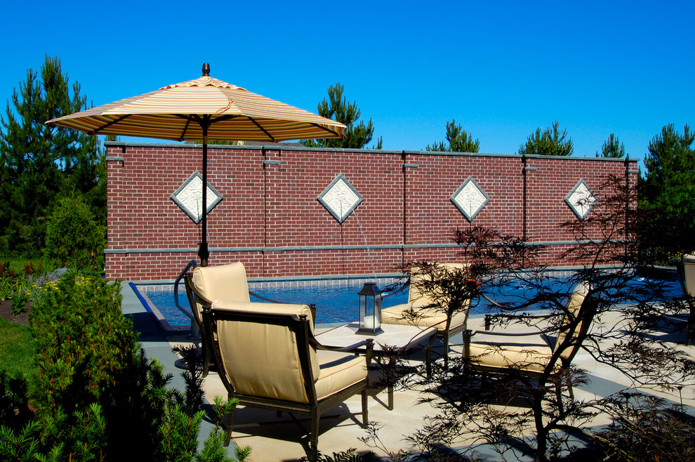 Modelo de piscina alargada mediterránea de tamaño medio rectangular en patio trasero con adoquines de piedra natural