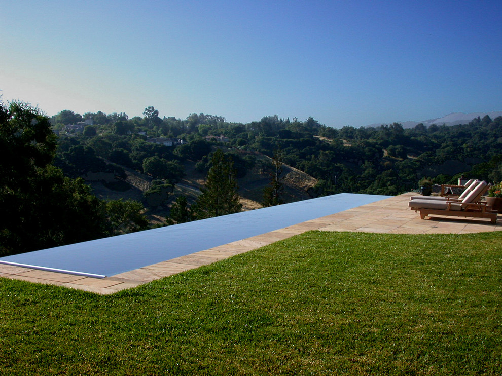 Diseño de piscina infinita tradicional grande rectangular en patio trasero con adoquines de piedra natural