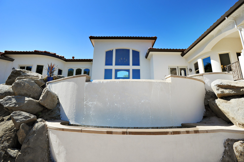 Idee per una piccola piscina a sfioro infinito mediterranea personalizzata dietro casa con fontane e lastre di cemento