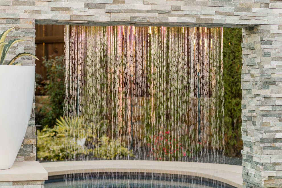Ejemplo de piscina con fuente alargada tradicional renovada grande a medida en patio trasero con losas de hormigón
