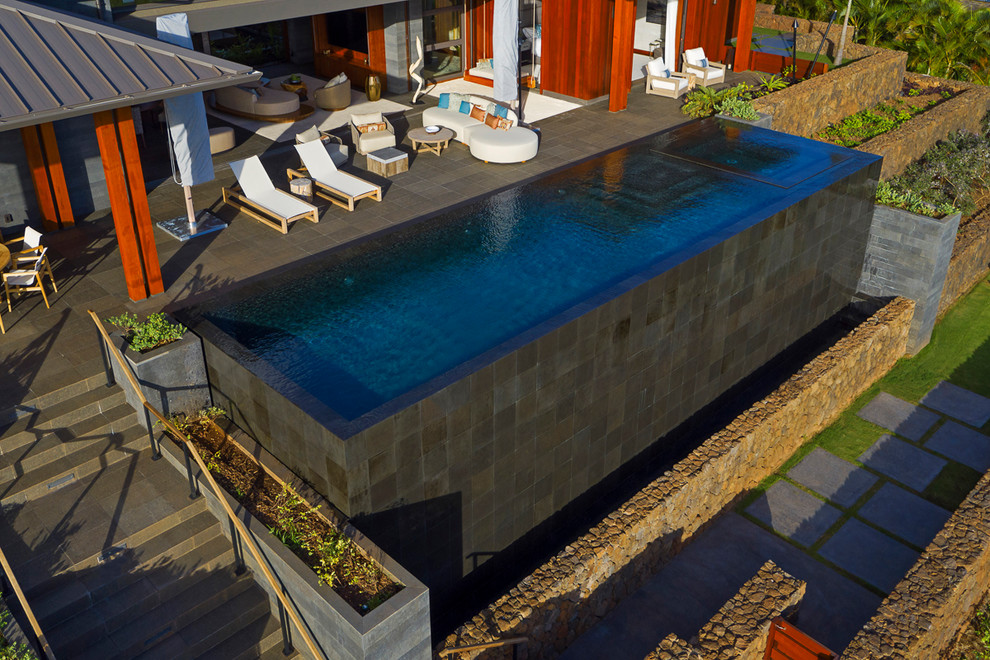 Foto de piscinas y jacuzzis infinitos tropicales de tamaño medio rectangulares en patio trasero con adoquines de piedra natural