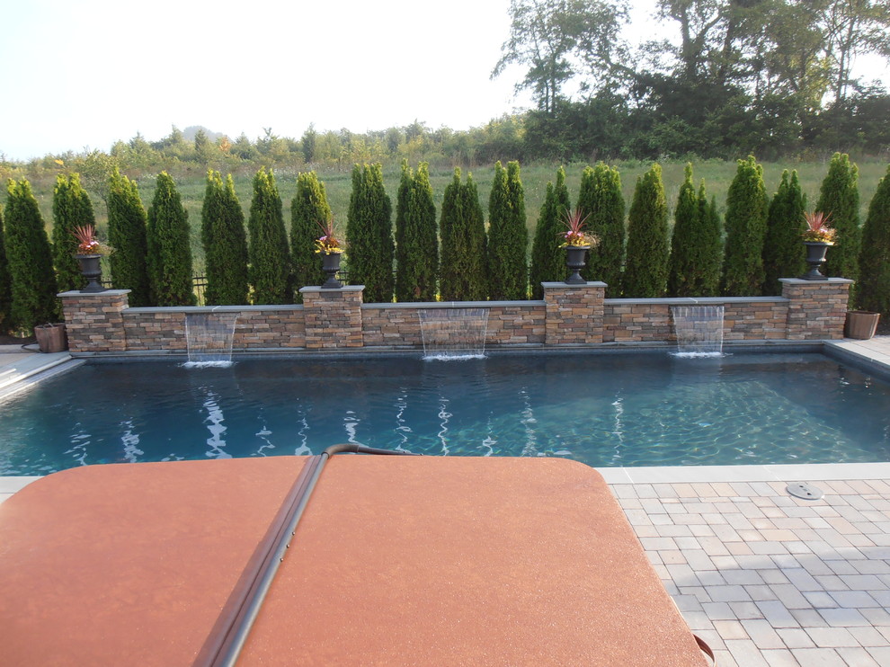 Modelo de piscina con fuente natural tradicional rectangular en patio trasero con adoquines de ladrillo