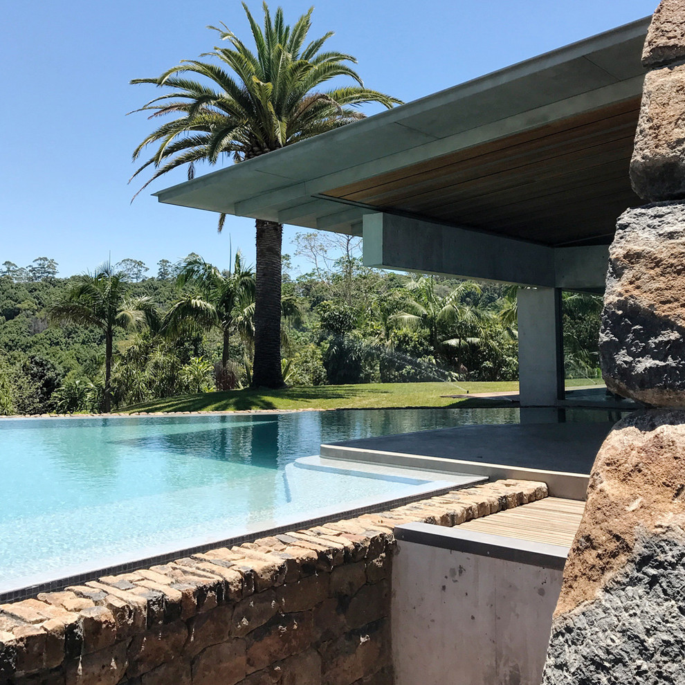 Imagen de piscina infinita grande en forma de L en patio lateral con adoquines de piedra natural