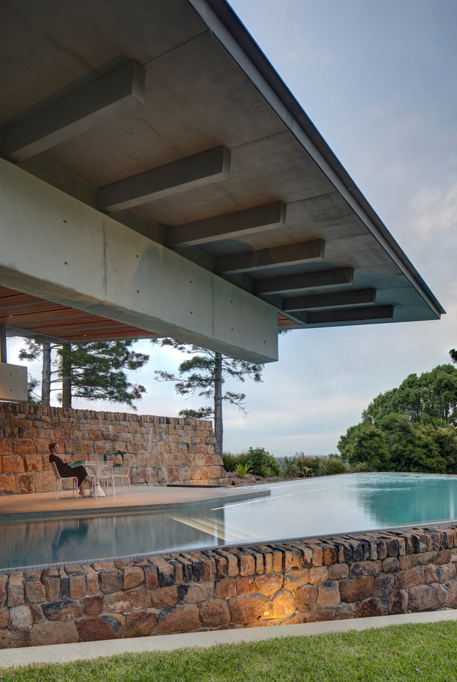 Ispirazione per una grande piscina a sfioro infinito moderna a "L" nel cortile laterale con pavimentazioni in pietra naturale