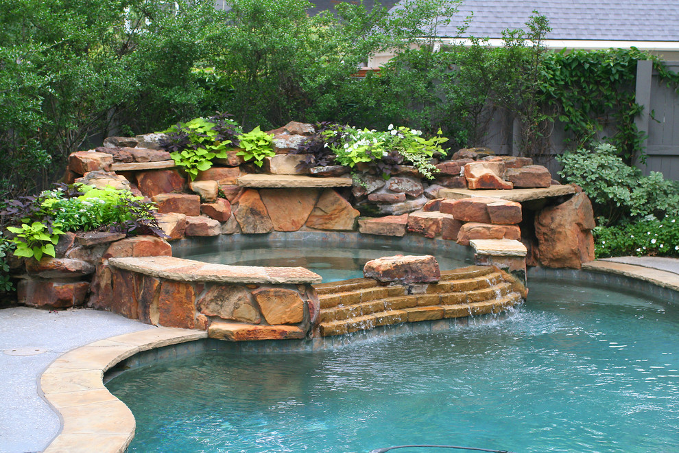 Cette image montre une grande piscine arrière traditionnelle sur mesure avec des pavés en pierre naturelle et un bain bouillonnant.