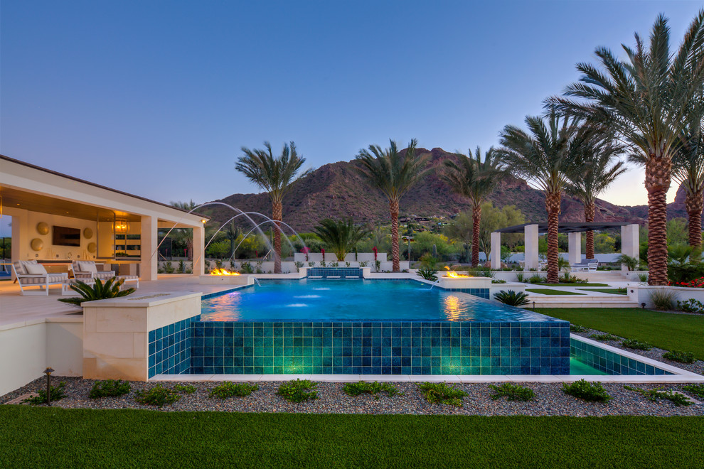This is an example of an expansive contemporary back rectangular infinity swimming pool in Phoenix with a pool house.