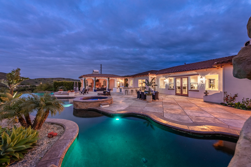 Imagen de casa de la piscina y piscina infinita mediterránea extra grande a medida en patio trasero con suelo de hormigón estampado