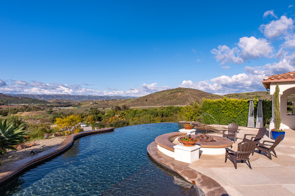 Immagine di un'ampia piscina a sfioro infinito mediterranea personalizzata dietro casa con una dépendance a bordo piscina e cemento stampato