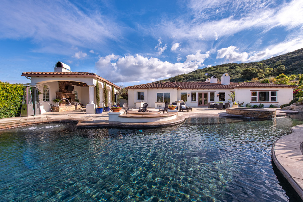 Пример оригинального дизайна: огромный бассейн-инфинити произвольной формы на заднем дворе в средиземноморском стиле с домиком у бассейна и покрытием из декоративного бетона