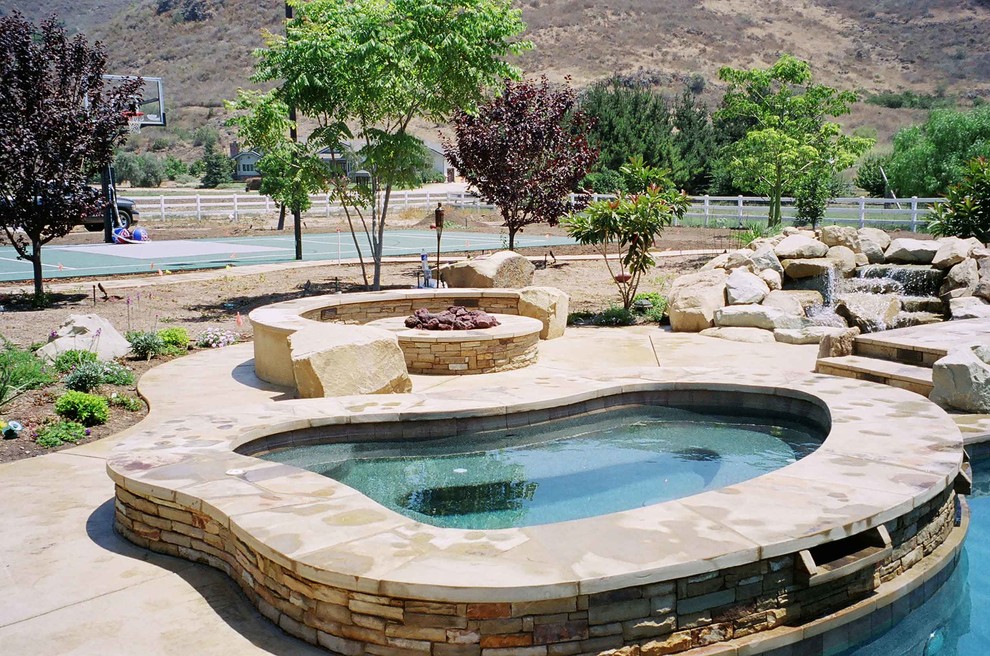 Exemple d'une grande piscine naturelle et arrière chic sur mesure avec un bain bouillonnant et des pavés en pierre naturelle.