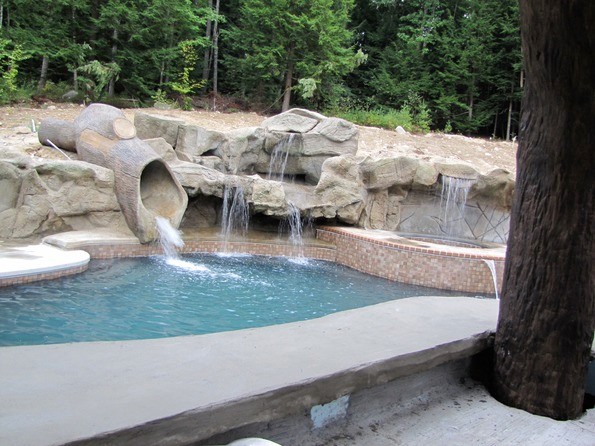 This is an example of a large rustic back custom shaped lengths swimming pool in Austin with a water slide and natural stone paving.