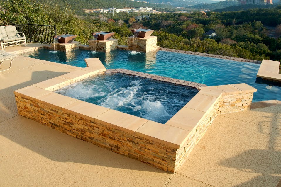 Exemple d'une grande piscine à débordement et arrière chic sur mesure avec un bain bouillonnant et une dalle de béton.