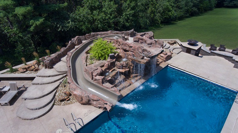Immagine di una grande piscina monocorsia tradizionale rettangolare dietro casa con un acquascivolo e pavimentazioni in cemento