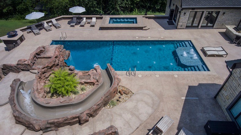 Modelo de piscina con tobogán alargada tradicional renovada extra grande rectangular en patio trasero con adoquines de hormigón