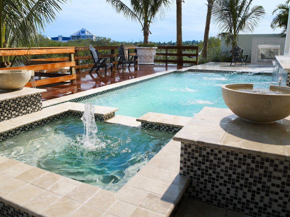 Immagine di una piscina monocorsia tropicale rettangolare di medie dimensioni e dietro casa con fontane e pavimentazioni in pietra naturale