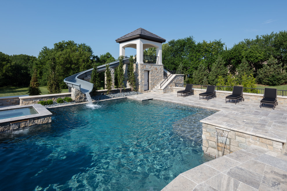 Ejemplo de piscina con tobogán clásica renovada extra grande a medida en patio trasero con adoquines de piedra natural