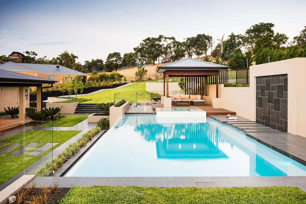 Diseño de piscina actual grande rectangular en patio trasero con adoquines de hormigón